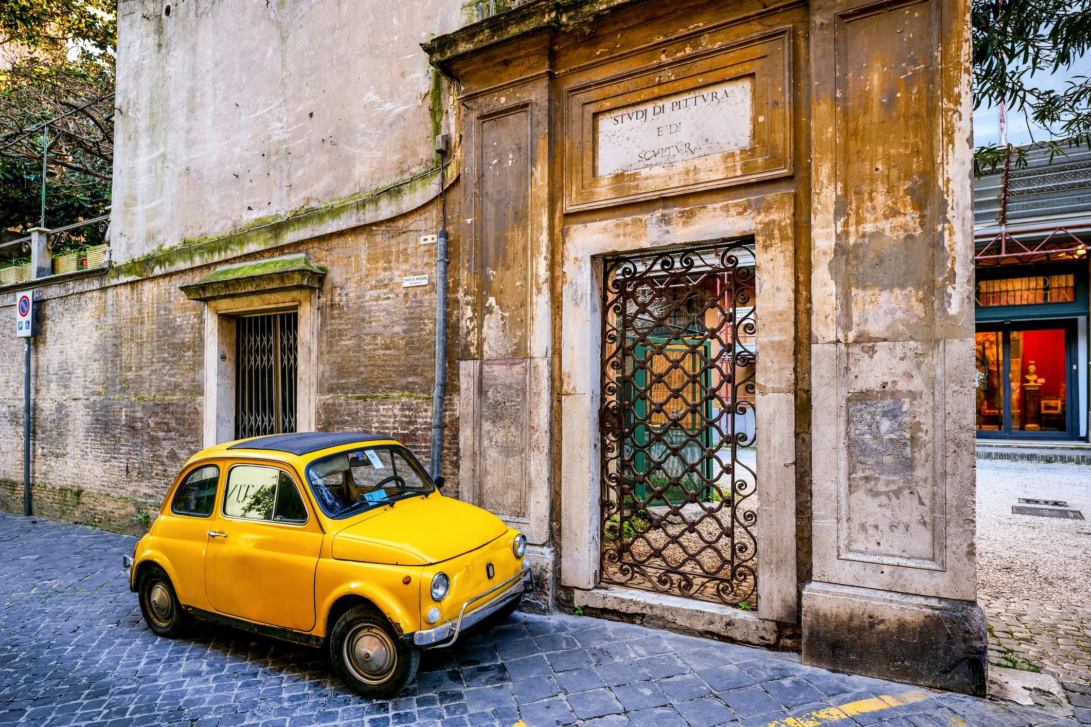 Vintage yellow Fiat 500 full-body shot parked along a stone alley