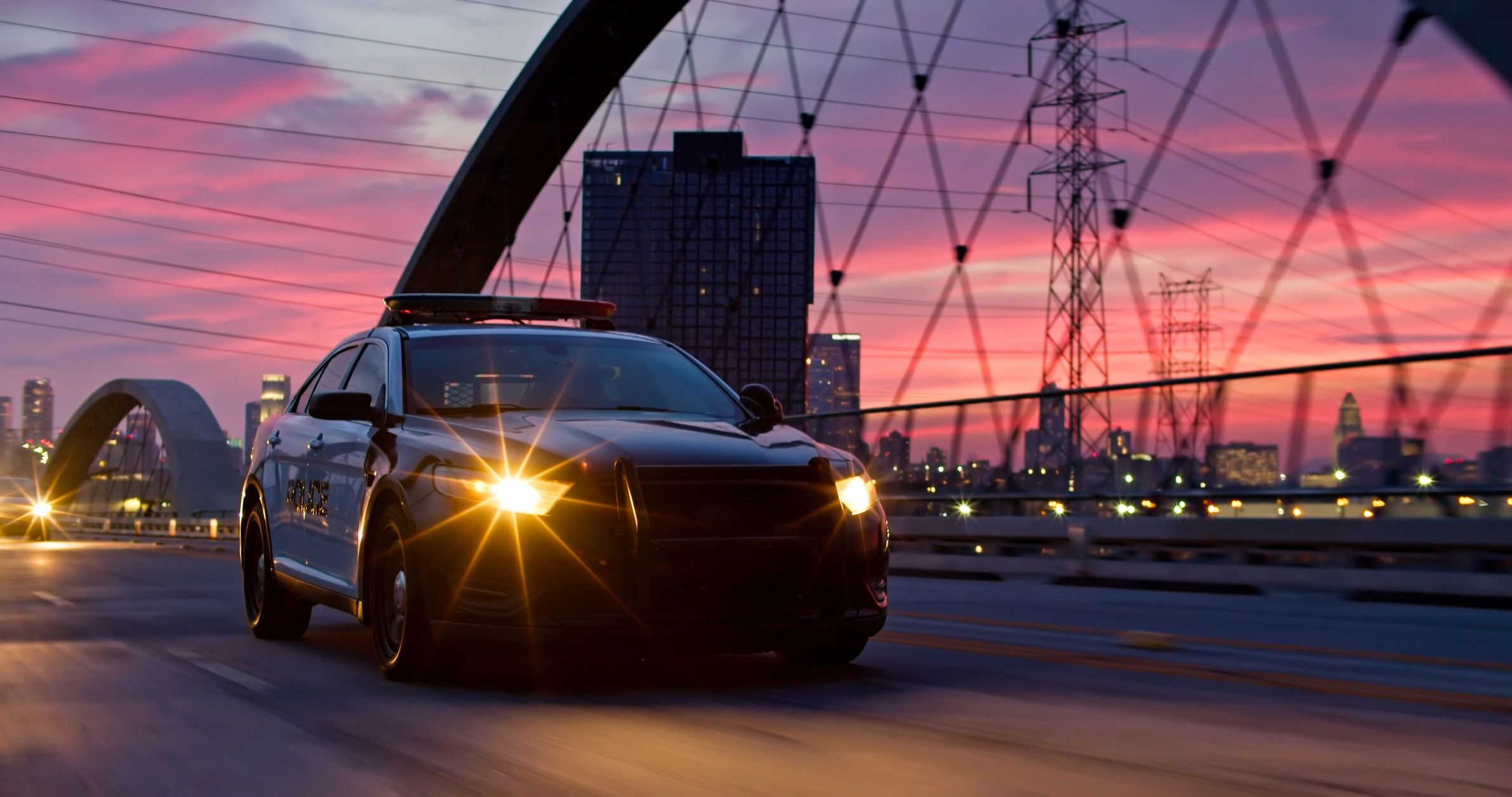 Car driving on a bridge at sunset with city skyline